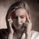 Services-Headaches Picture of woman with closed eyes and a pained look on her face. She is massaging her temples with fingers from both hands.